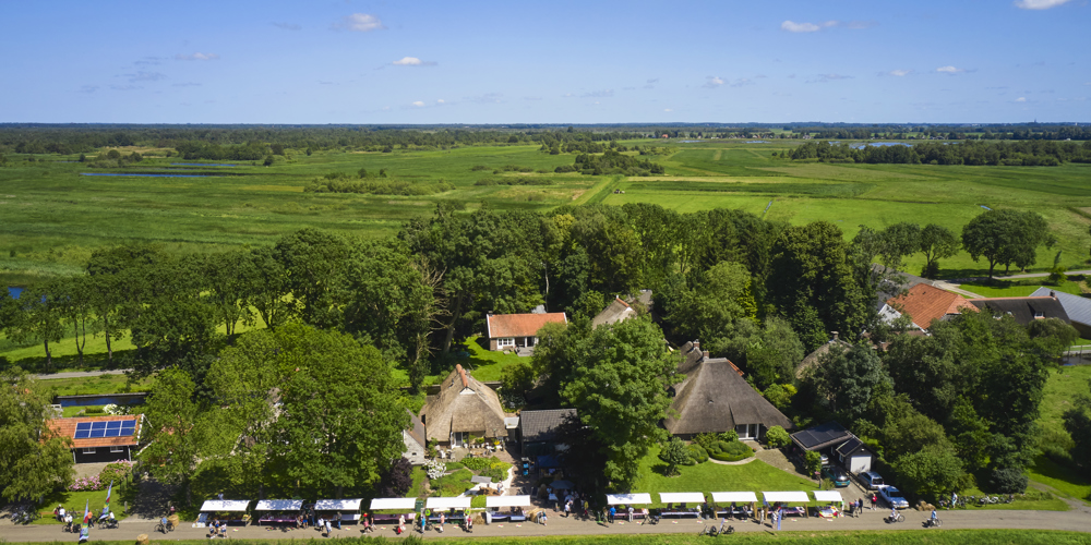 vogel perspectief foto van landschap met bomen en op voorgrond witte kraampjes met mensen op een lange strook weg