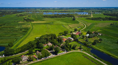 vogel perspectief foto van landschap met bomen en op voorgrond witte kraampjes met mensen op een lange strook weg