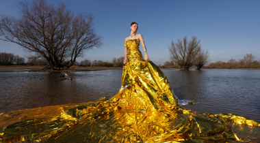 Persoon in een grote gele kunstzinnige jurk gemaakt van plastic in een natuurgebied met water en bomen