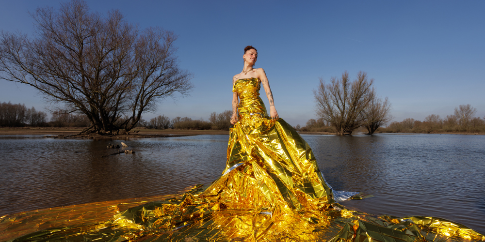 Persoon in een grote gele kunstzinnige jurk gemaakt van plastic in een natuurgebied met water en bomen