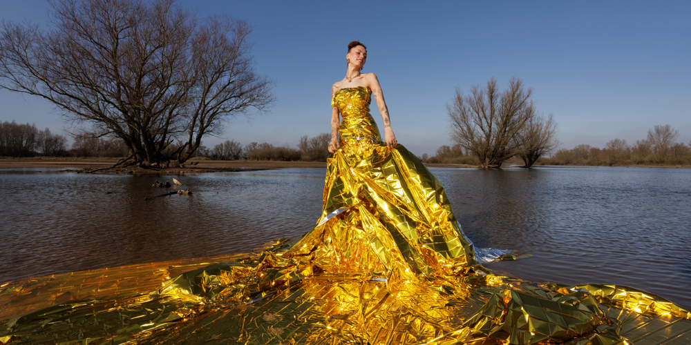 Persoon in een grote gele kunstzinnige jurk gemaakt van plastic in een natuurgebied met water en bomen