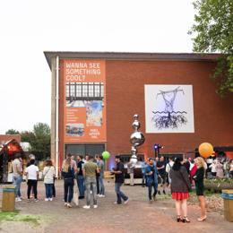 Groep mensen bij ingang van de Koelwaterhal met kunst en aankondigingsbanner op de gevel