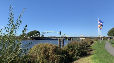 Zwartewaterbrug over het water, 3 vlaggen aan de rechterkant, struiken en een fietspad