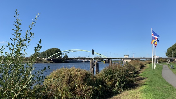 Zwartewaterbrug over het water, 3 vlaggen aan de rechterkant, struiken en een fietspad