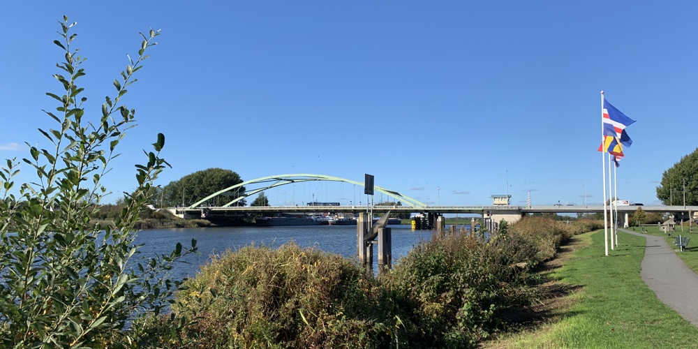 Zwartewaterbrug over het water, 3 vlaggen aan de rechterkant, struiken en een fietspad