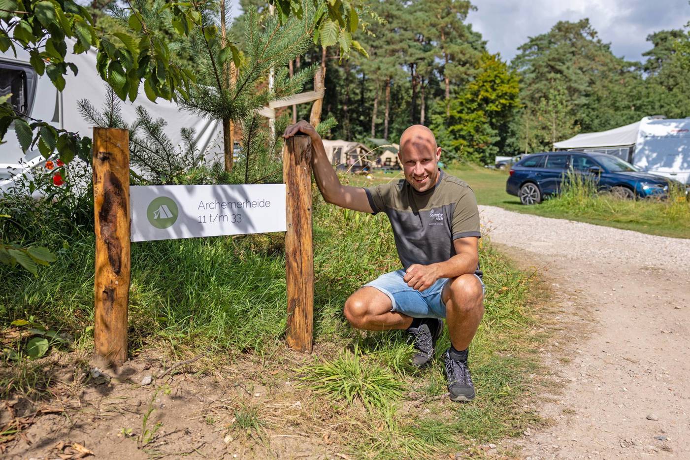 Man knielt naast een houten bord met de tekst "Archemerheide 11 t/m 33" op een campingterrein.