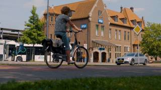 Fietser rijdt langs station Deventer met bussen en auto’s op de achtergrond.