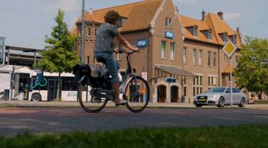 Fietser rijdt langs station Deventer met bussen en auto’s op de achtergrond.