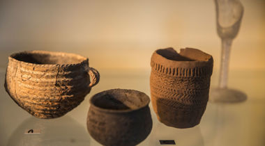 Oude stenen potten in een glazen vitrine met toegekende etiketjes met letters erop in museum