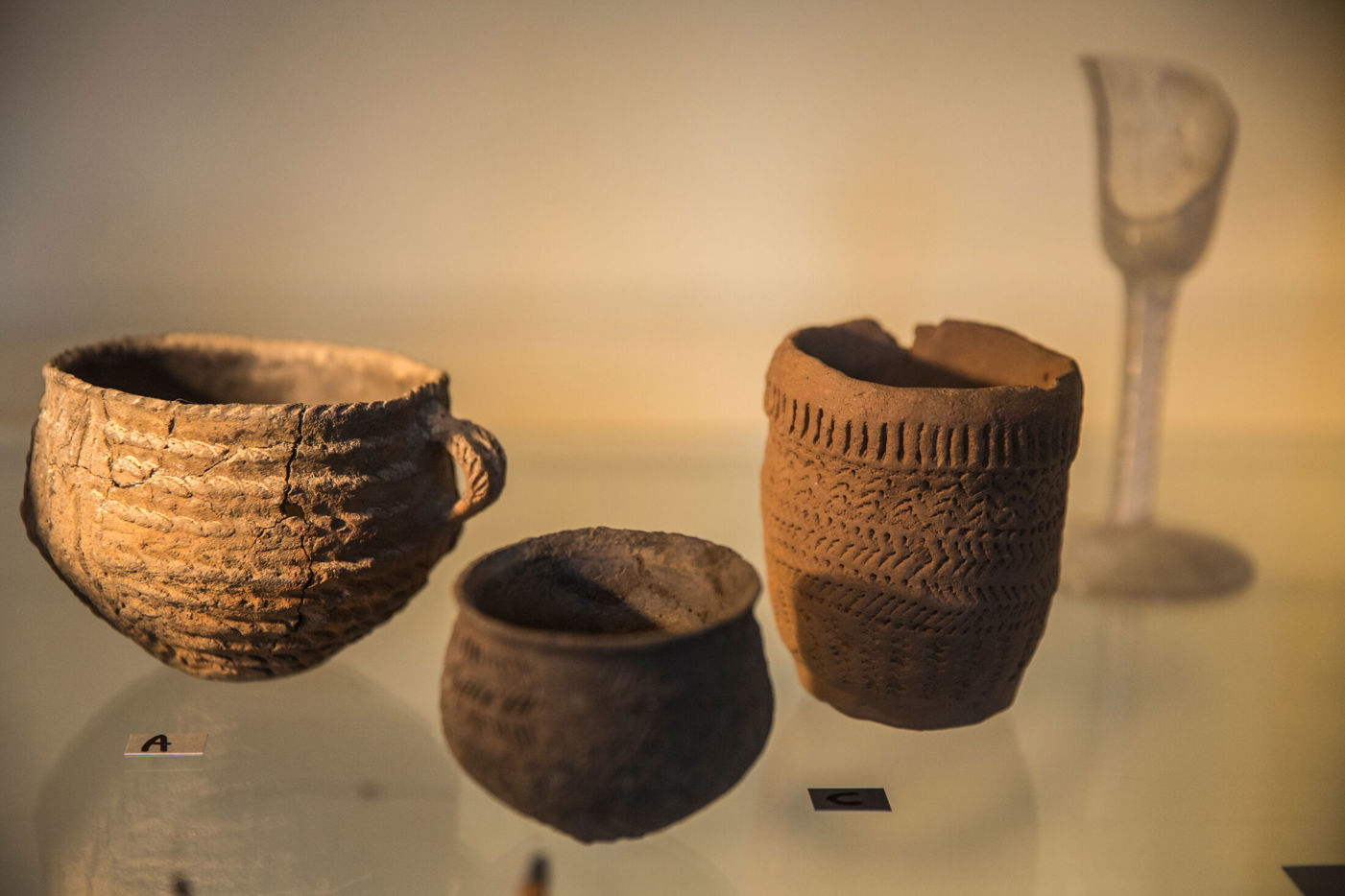 Oude stenen potten in een glazen vitrine met toegekende etiketjes met letters erop in museum