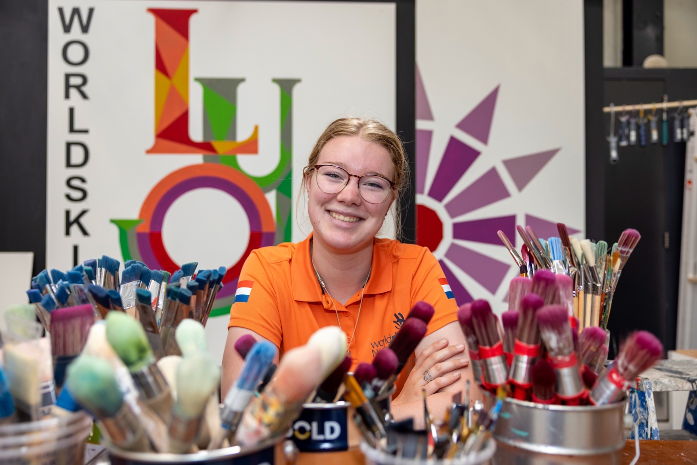 Sophie in haar oranje shirt voor een banner van het WK schilderen. Voor haar in beeld staan veel verschillende kwasten en pencelen.