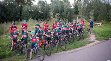 Groep met fietsers in helm en tenu langs weg in hoog gras