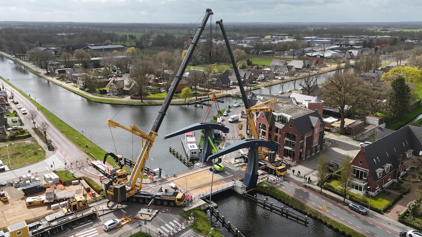 De brug gezien vanuit de lucht terwijl 2 hijskranen bezig zijn met het bewegende deel van de brug dat hier nog niet uit de brug is gehesen.