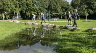kinderen spelen in een speeltuin met veel groen en grote speelstenen