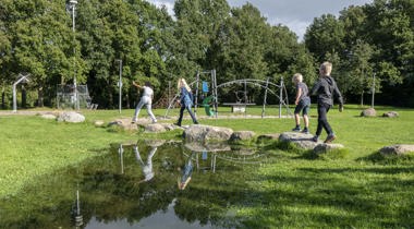 kinderen spelen in een speeltuin met veel groen en grote speelstenen