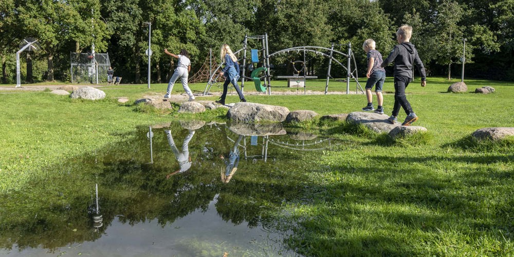 kinderen spelen in een speeltuin met veel groen en grote speelstenen