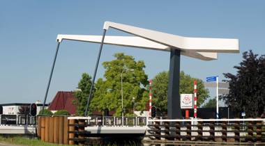 Moderne witte ophaalbrug over een kanaal bij een dorpsstraat.
