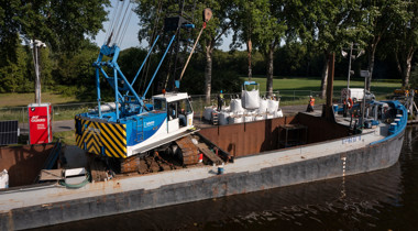 zicht op een boot met kraan die voor de damwand belastingsproef een tweede laag big bag zandzakken plaatst direct langs kanaal Almelo- De Haandrik