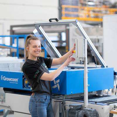 Een persoon bedient een blauwe industriële machine van het merk Growcoon in een moderne fabriekshal.