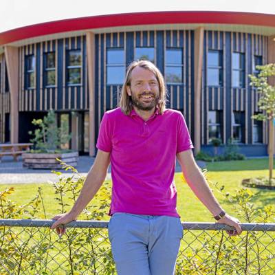 Luc Lenferink poseert leunend tegen een laag hek voor het bedrijsgebouw van Uw Onderhoudspartner Lenferink