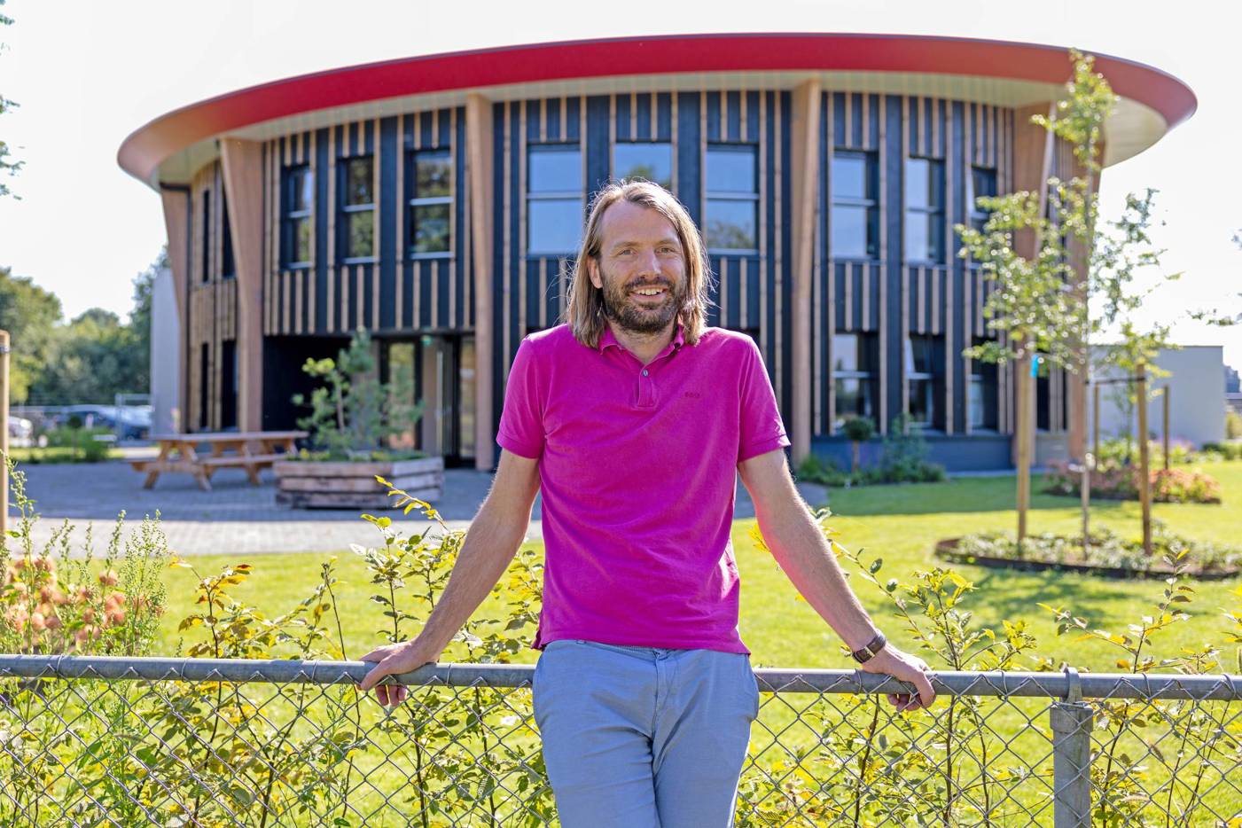 Luc Lenferink poseert leunend tegen een laag hek voor het bedrijsgebouw van Uw Onderhoudspartner Lenferink