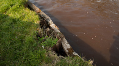 Foto van houten muur tussen sloot en groene oever