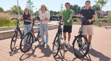 Vier scholieren staan op een zonnig plein naast hun fiets