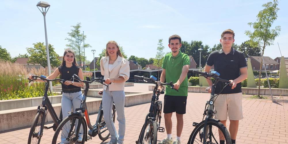 Vier scholieren staan op een zonnig plein naast hun fiets