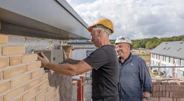 Twee mensen met witte werkhelmen zetten grijze baksteen tussen muur