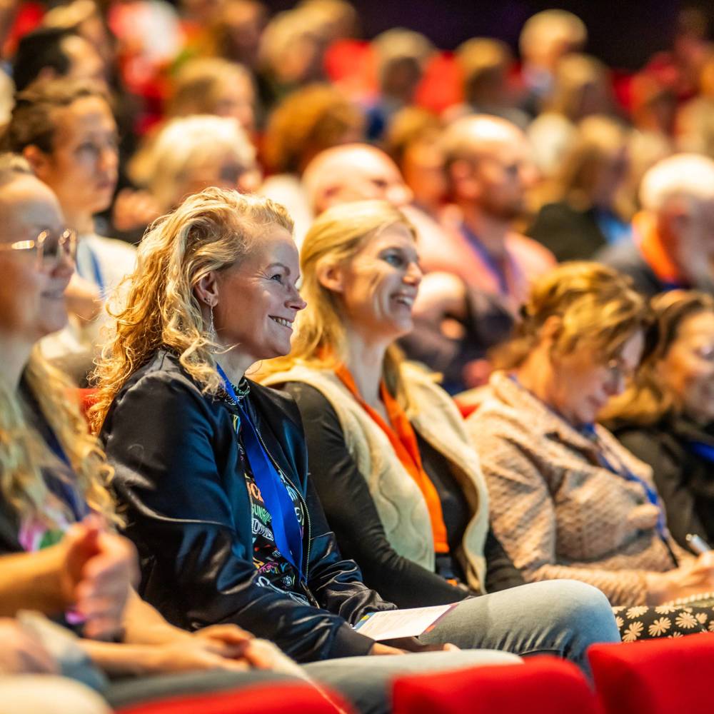 Een grote groep mensen zit in een auditorium en luistert aandachtig naar een spreker tijdens het Vrijwilligerscongres.