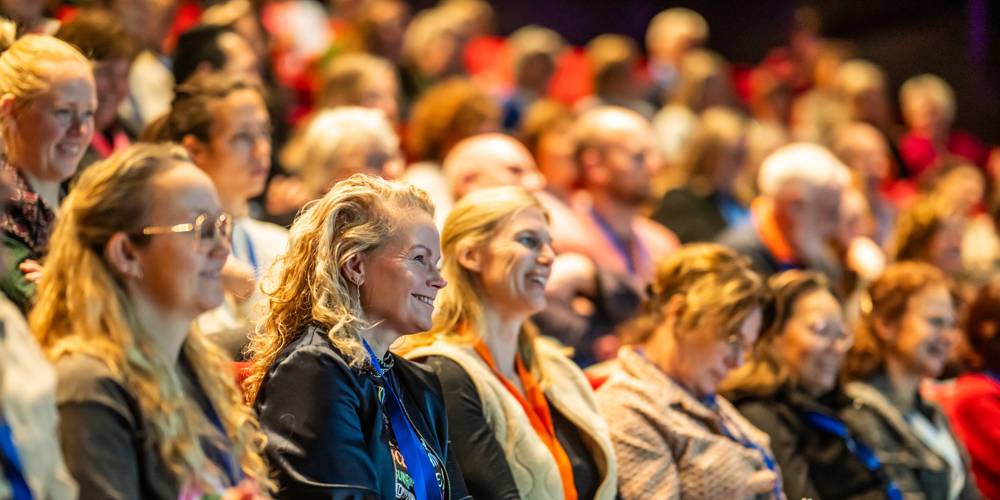 Een grote groep mensen zit in een auditorium en luistert aandachtig naar een spreker tijdens het Vrijwilligerscongres.