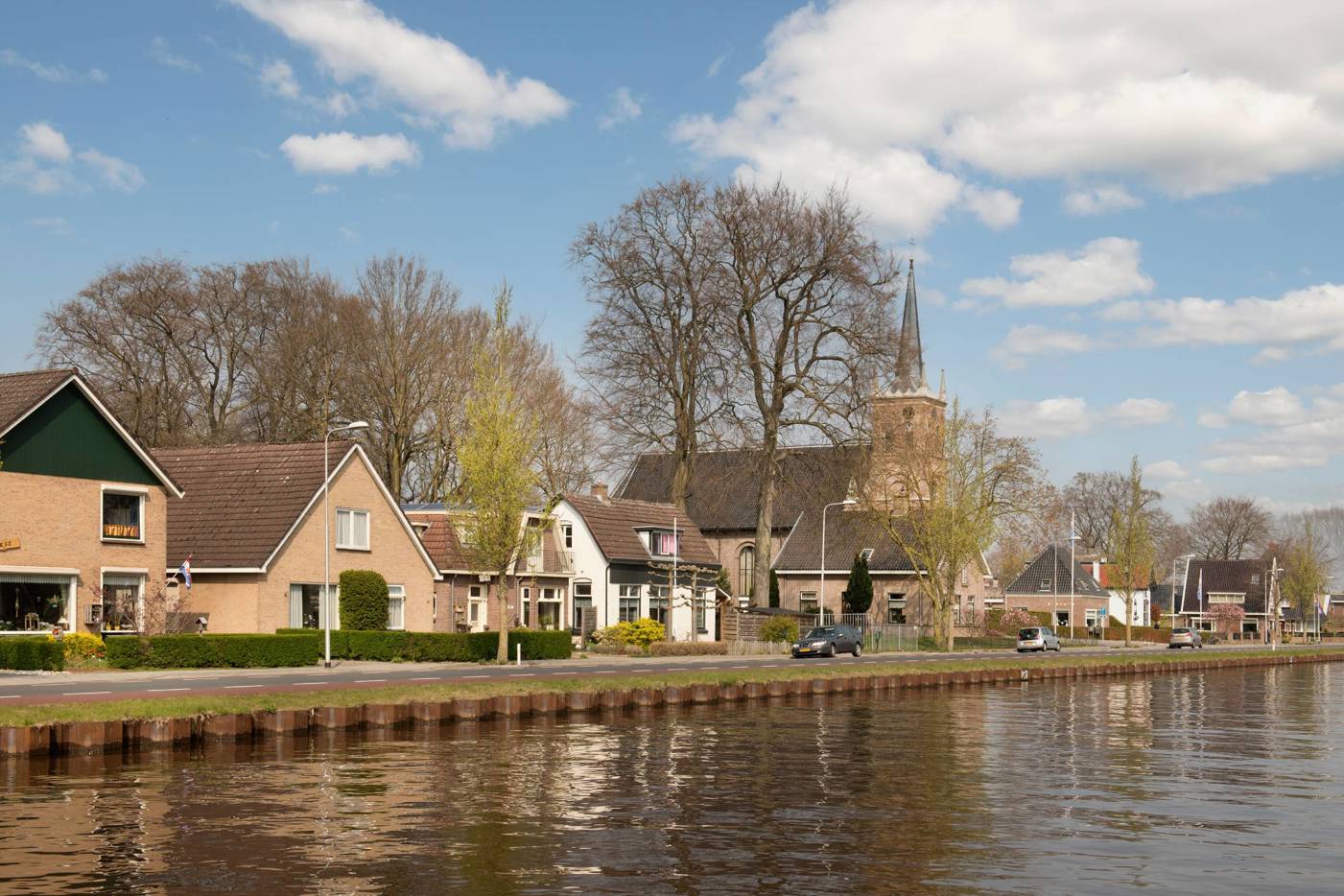 Kanaal met dorpshuizen en kerk in een rustige lentesfeer.