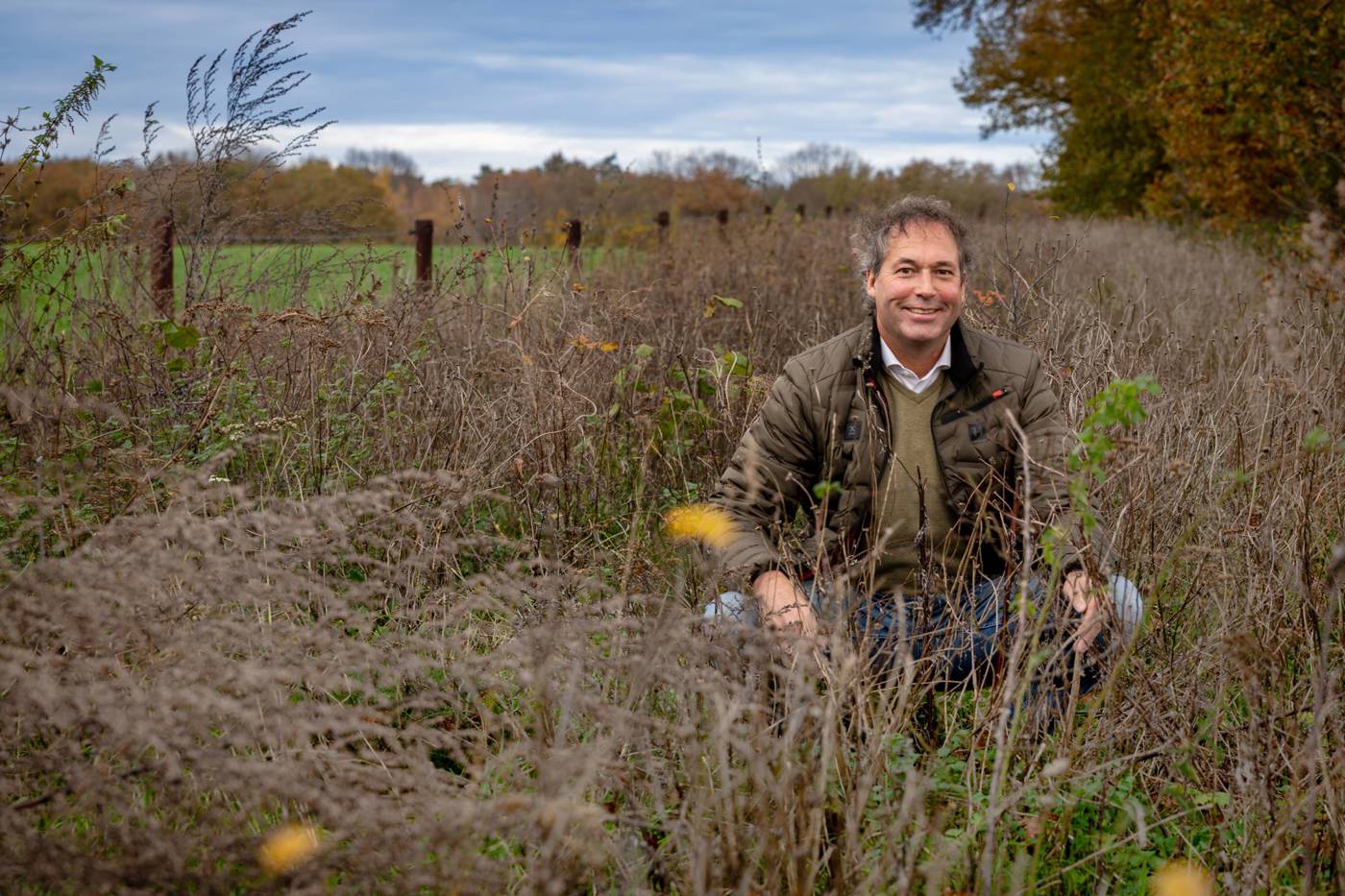 Man zit in een veld met hoge, droge planten in een herfstlandschap.