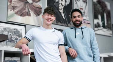 Twee vrijwilligers poseren. Ze kijken lachend in de lens.