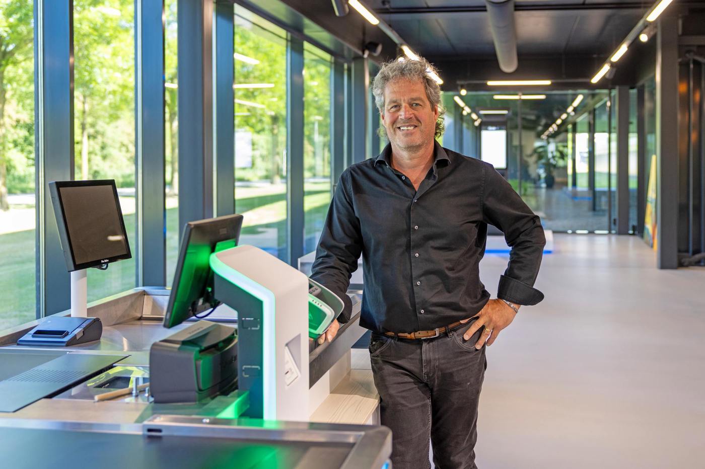 Heico Booijink bij zelfbedieningskassa in moderne, lichte ruimte met grote ramen.