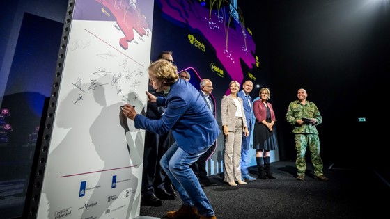 Een groep mensen poseert op een podium voor een groot scherm met de tekst “Intentieverklaring Regionale Innovatiesamenwerking” en een kaart van Nederland met logo’s van regionale ontwikkelingsmaatschappijen.