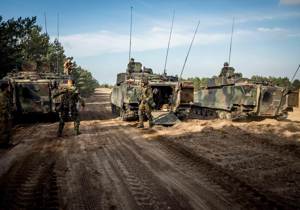 Mensen in militair kostuum op modderige grond met tanks