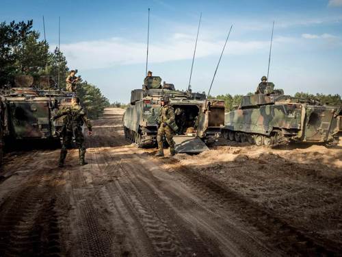 Mensen in militair kostuum op modderige grond met tanks