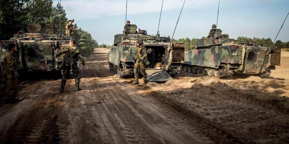 Mensen in militair kostuum op modderige grond met tanks