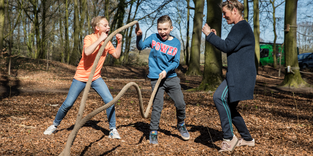 Drie mensen in het bos waarvan eentje aan touwen schudt