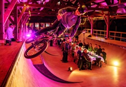 Vrijwilligersprijs. Lange tafel waar mensen een etentjes hebben. Dit alles op een soort bmx baan in een hal.