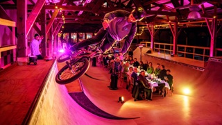 Vrijwilligersprijs. Lange tafel waar mensen een etentjes hebben. Dit alles op een soort bmx baan in een hal.