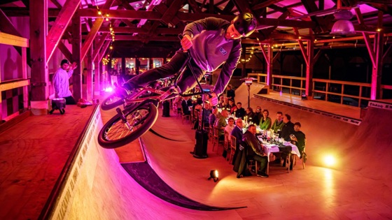 Vrijwilligersprijs. Lange tafel waar mensen een etentjes hebben. Dit alles op een soort bmx baan in een hal.