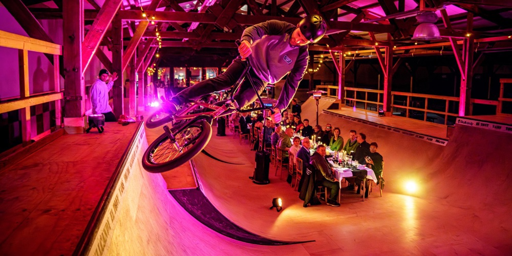 Vrijwilligersprijs. Lange tafel waar mensen een etentjes hebben. Dit alles op een soort bmx baan in een hal.