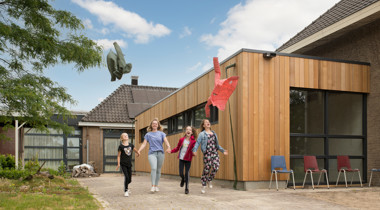 Vier mensen hand in hand huppelen voor gebouw