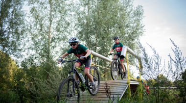 Twee fietsers fietsen over houten brug tussen hoog gras en bomen