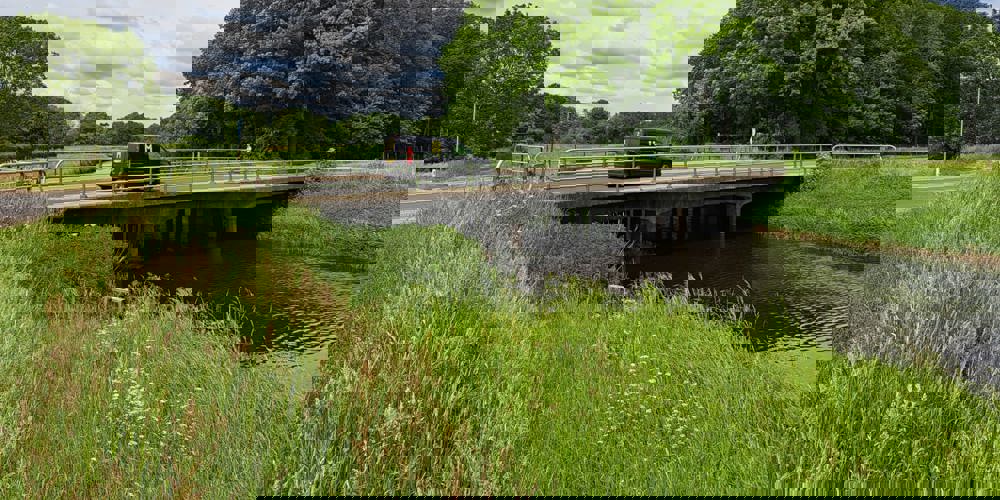 Auto die rijdt over bruggetje tussen groen landschap
